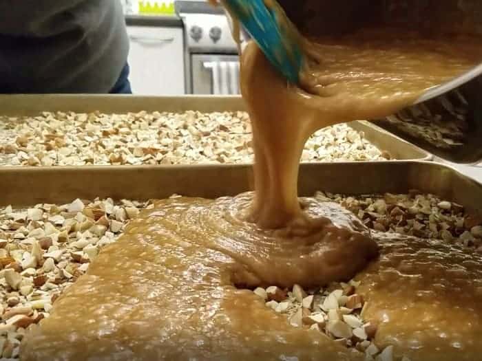 Pouring homemade english toffee mixture over chopped almonds.