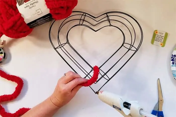 Gluing red fluffy yarn to heart-shaped wire wreath form.