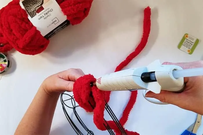 Wrapping and gluing red fluffy yarn to bottom point of heart-shaped wire wreath.