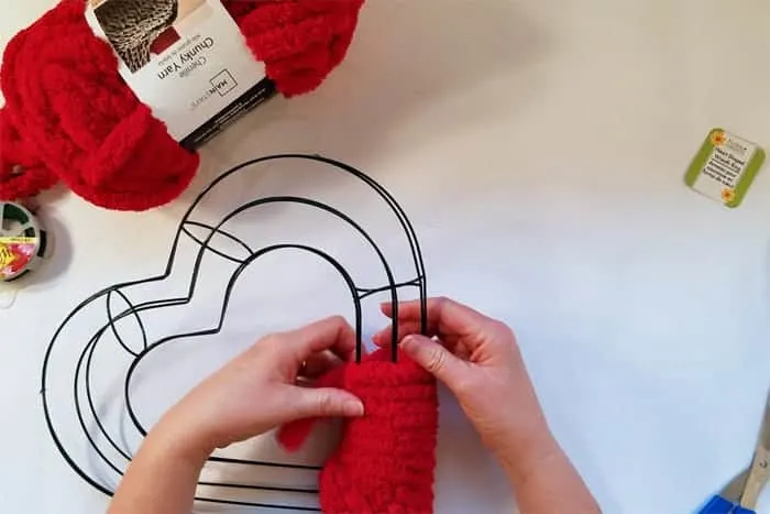 Wrapping red fluffy yarn around heart-shaped wire wreath form.
