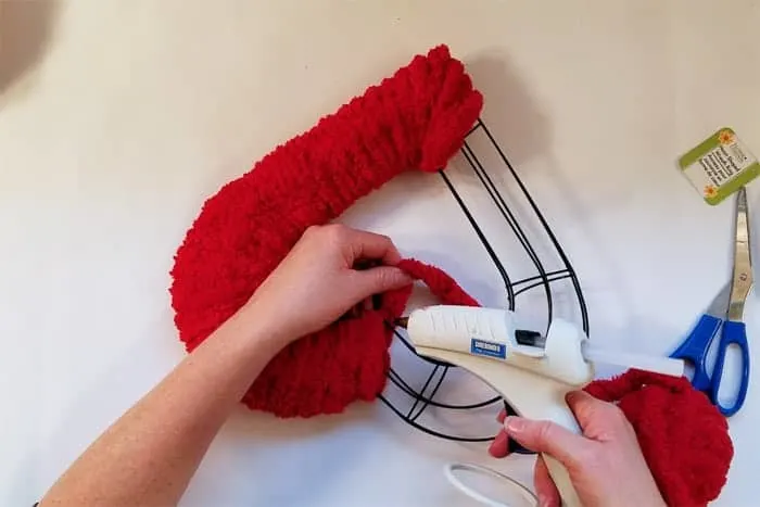 Gluing red fluffy yarn into point of wire heart valentine wreath.