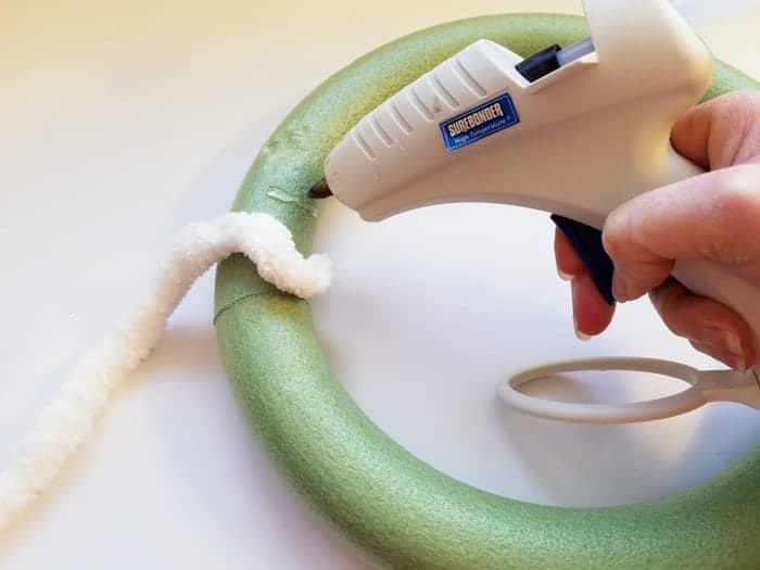 Adding dollop of hot glue to green wreath form to attach white fluffy yarn.