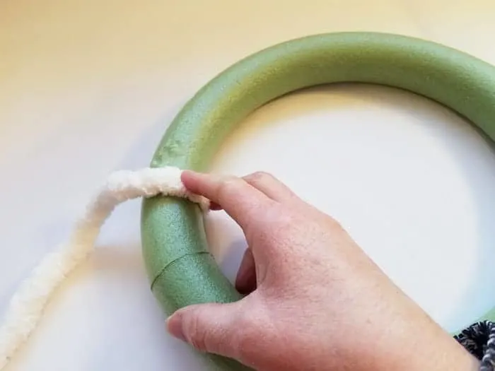 Pressing chenile yarn onto hot glue on green wreath form.