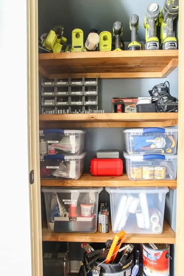 Garage tools and bins on wood shelves in closet.
