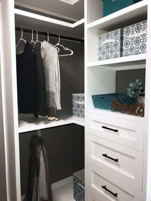 White closet Organizing system with clothes hanging and colored boxes on shelves.