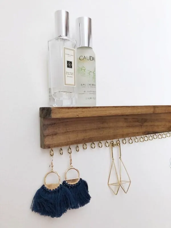 Narrow shelve with perfume on top and earrings hung on hooks below.