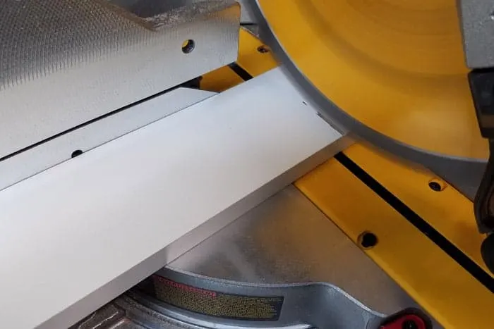 Miter saw blade cutting into white board for vinyl storage rack