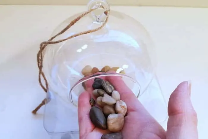 Inserting pebbles into hanging terrarium by hand.