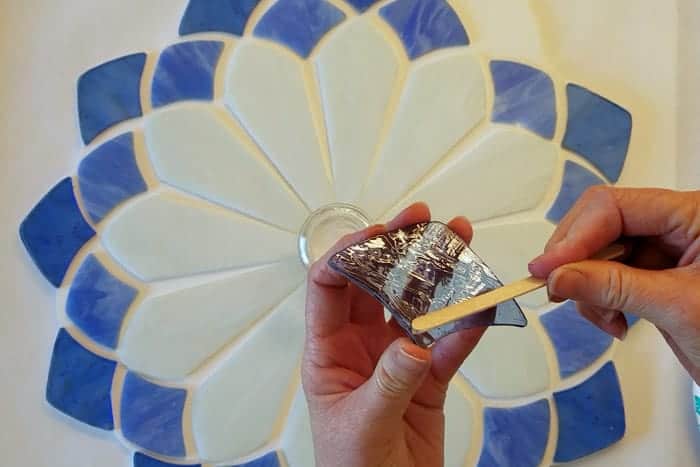 Applying clear glue with a craft stick to the back of stained glass piece.