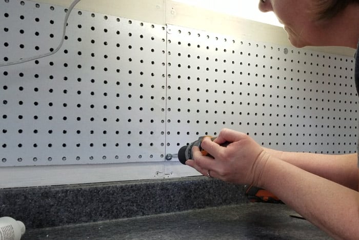 Screwing pegboard to the wood frame with cordless drill.