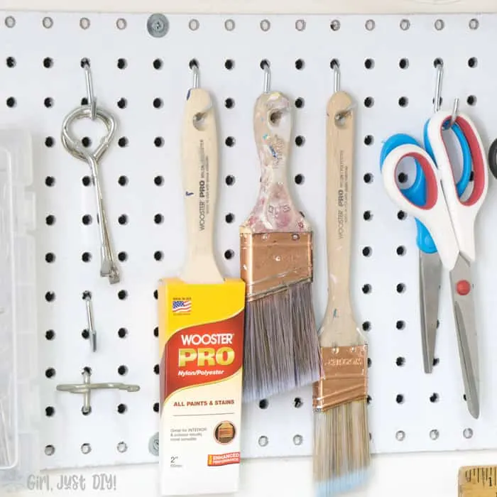 Paint brushes and scissors hanging on pegboard.