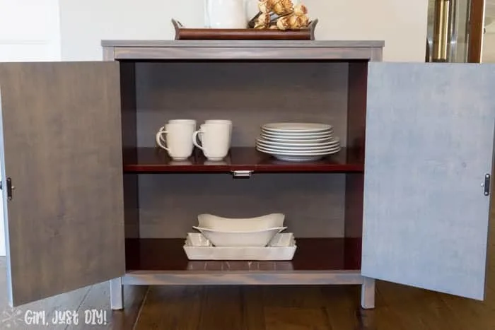 Chevron storage cabinet with doors open and dishes inside.