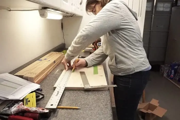 Woman drawing line on green tape on cabinet side panel.