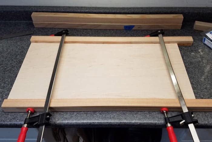 Two bar clamps holding side pieces of cabinet together.