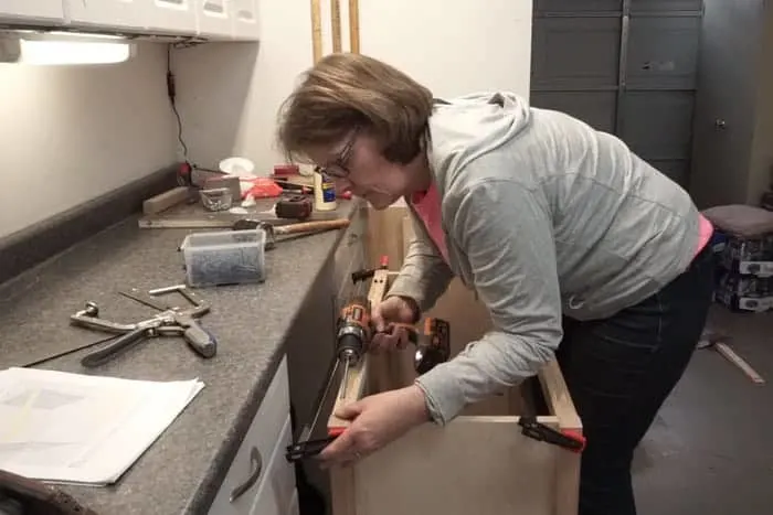 Woman attaching screws to cabinet build with cordless drill.