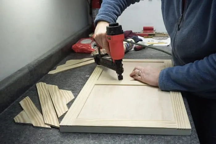 Brad nailer attaching trim to front of cabinet door.