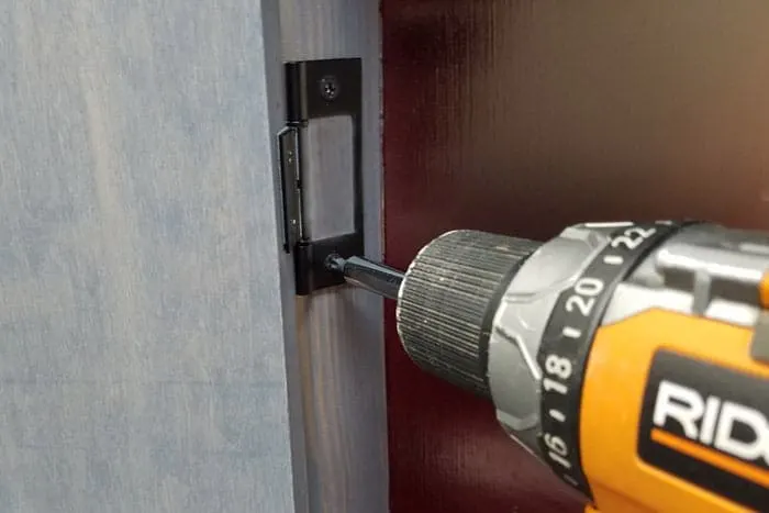 Cordless drill attaching hinges to chevron storage cabinet.