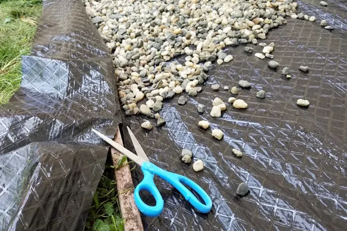 Using scissors to trim edges of weed block being held down with rocks.