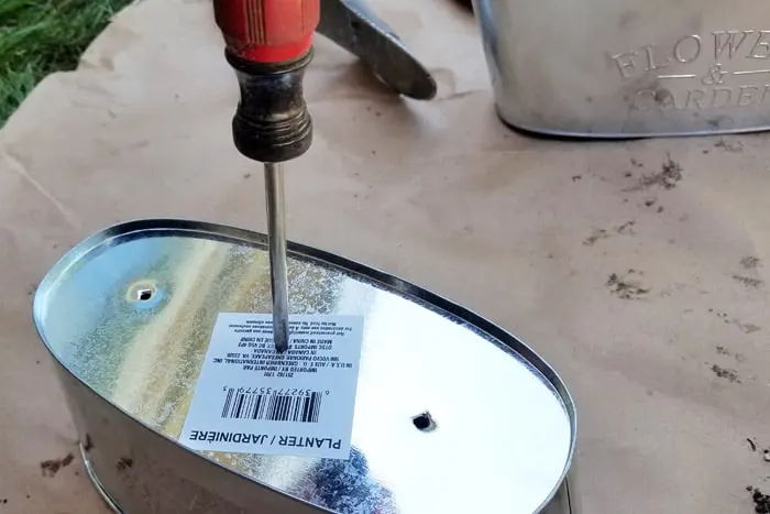 Punching holes in bottom of tin flower pot with a scratch awl for use in flower bed.