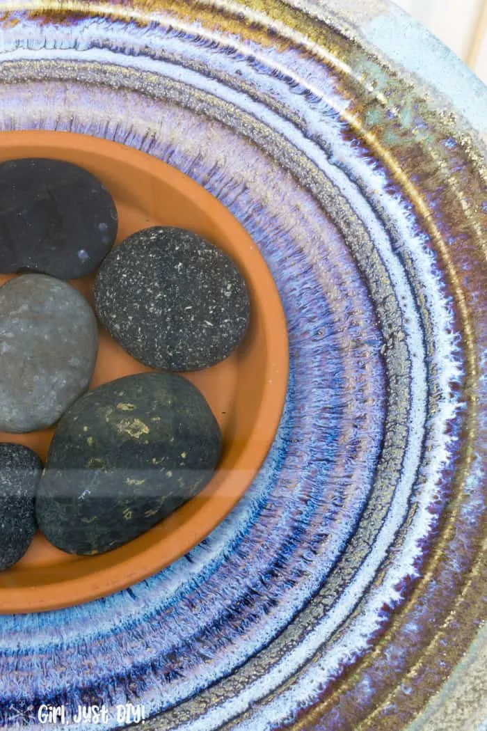 Blue and purple center of birdbath filled with water and blue mexican rocks.