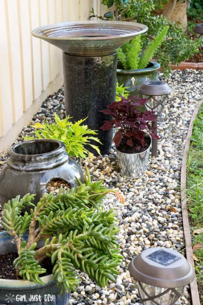 Completed weed-free rock flower bed with birdbath and flower pots.