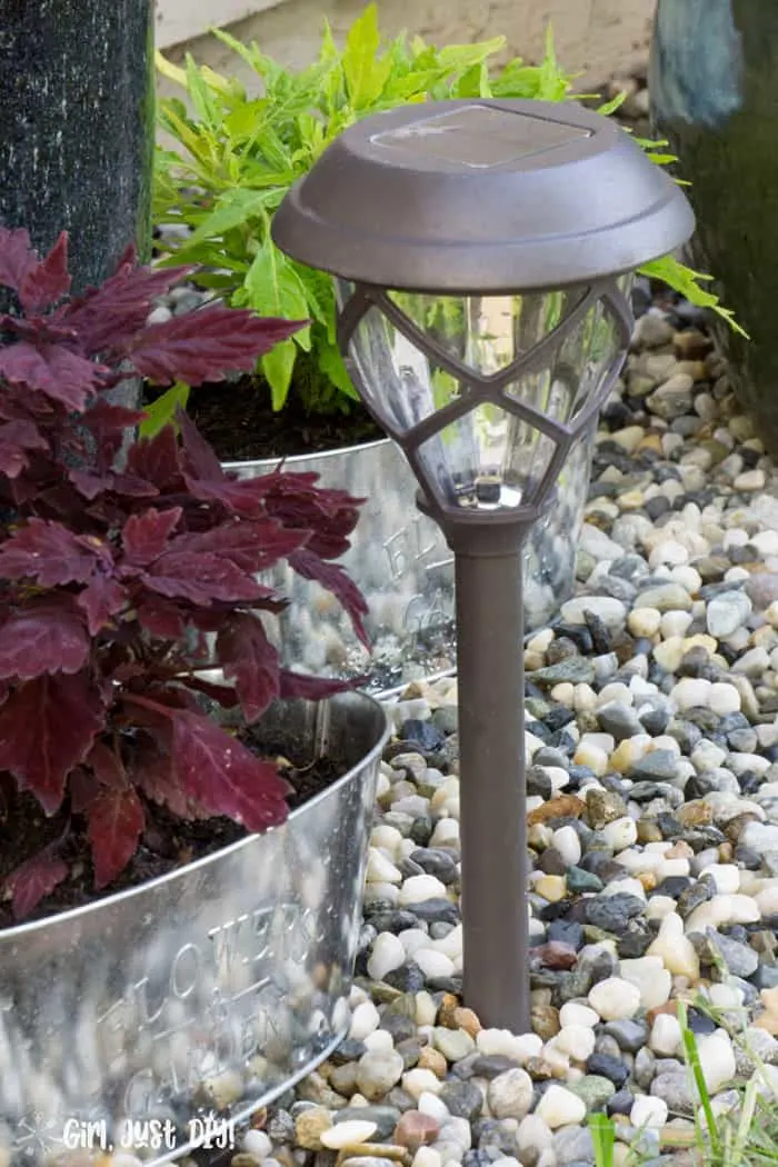 Solar path light next to coleus plant in rock flower bed.