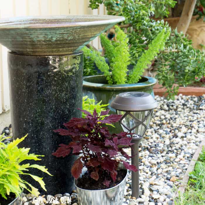 Birdbath with potted plants on rock flower bed.