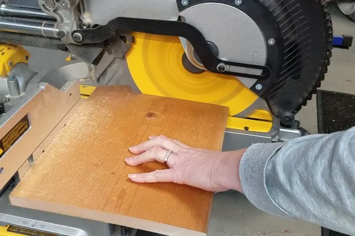 Cutting 1x10 board on miter saw for DIY footrest construction.