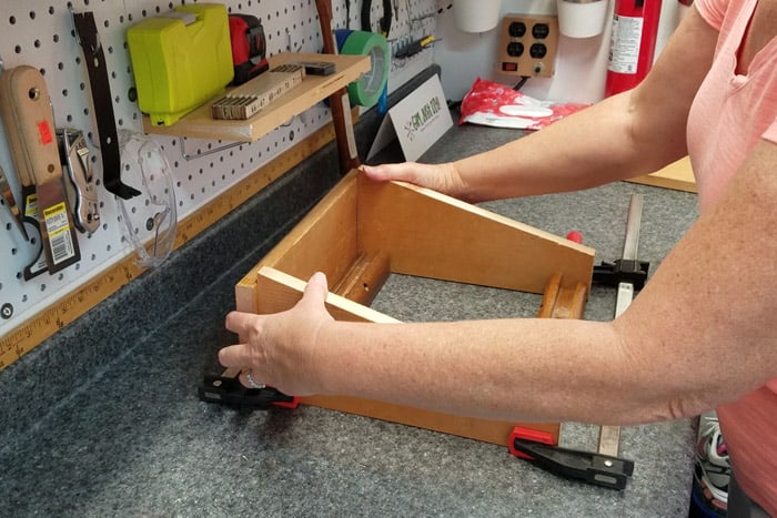 Clamps holding legs evenly spaced apart lwith hands holding a board  at back to get them square.