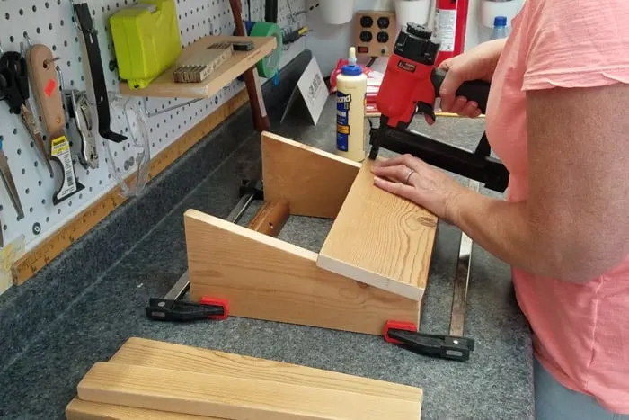 Holding a brad nailer to attach one of the top boards on footrest.