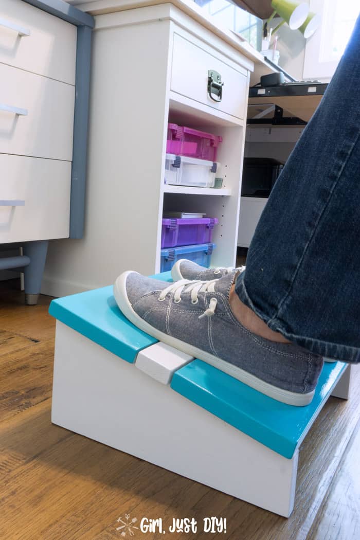 Blue tennis shoe feet on blue and white diy footrest in front of desk with colorful containers.