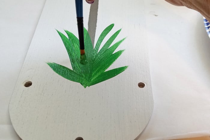 Freehand painting grass at base of birdhouse.