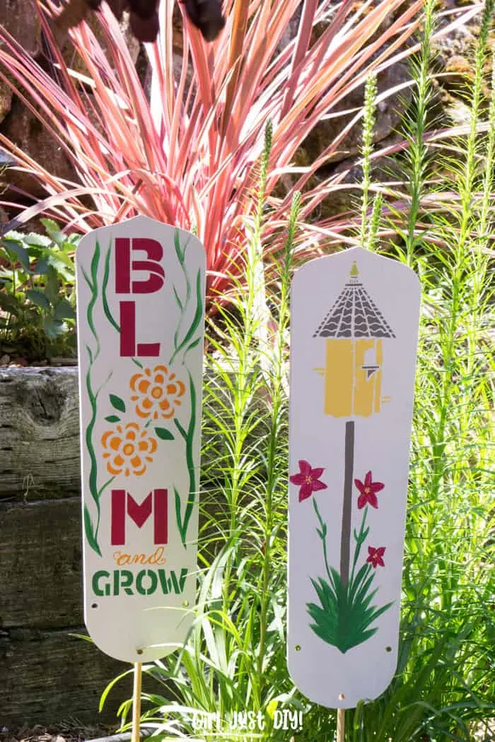 DIY Garden Signs from fan blades in front of tall greenery in garden.
