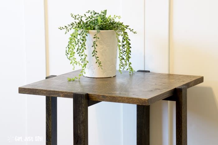 Wide picture of end table topped with houseplant in white pot showing wood tone contrasts.