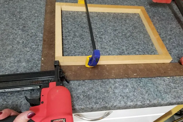 Clamped wood against framing square getting brad nailed.