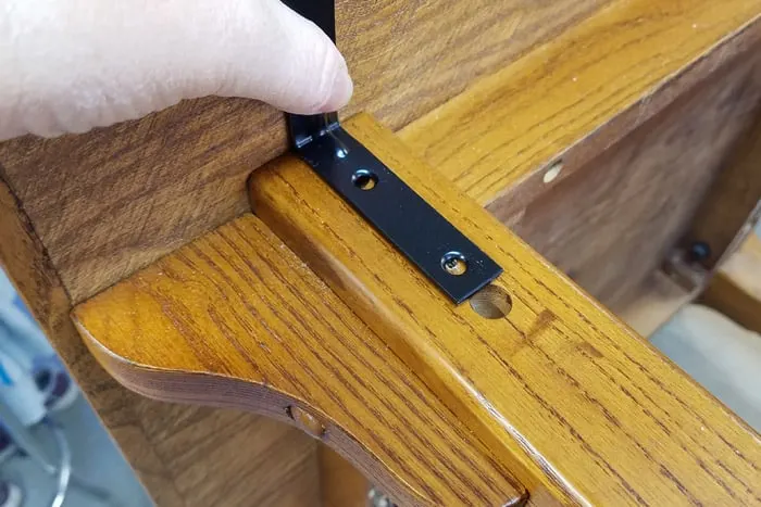 Black L bracket on table leg held by female hand.