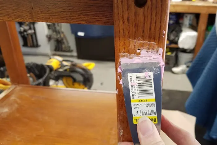 Female holding putty knife filling holes in table leg with spackle.