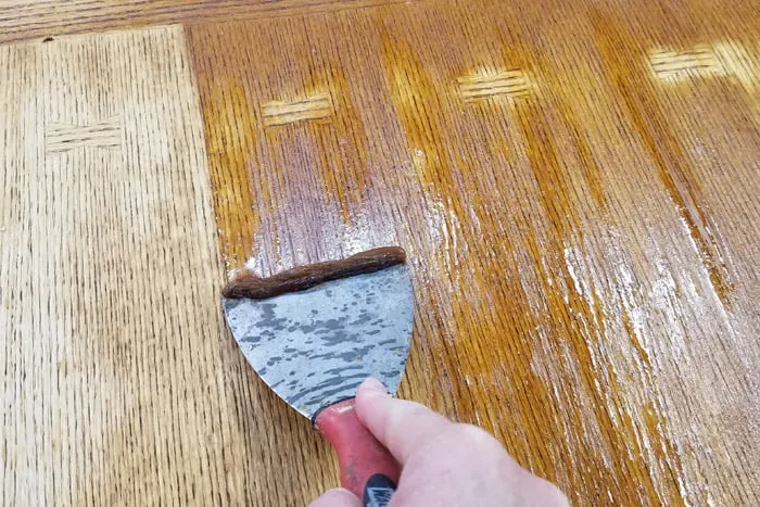 woman holding wide putty knife scraping stripper off table top.