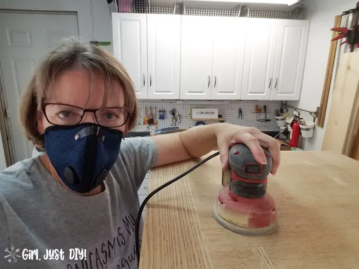 Woman wearing dust mask sanding a table top with orbital sander.