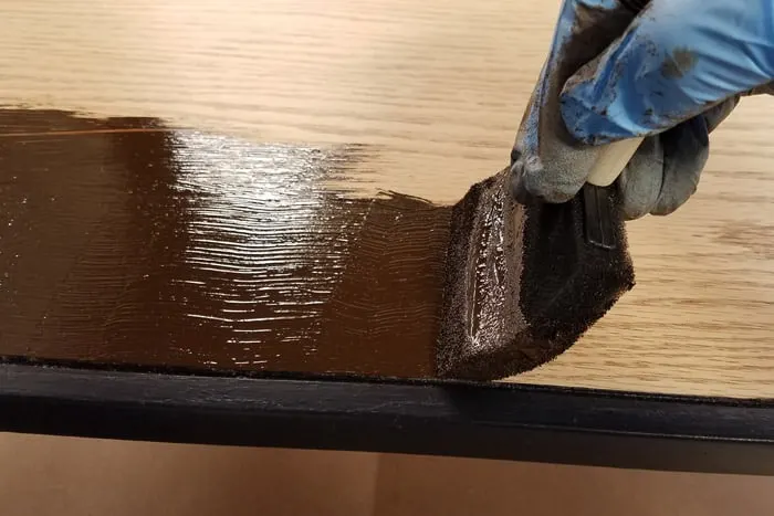 Brown stain being applied with foam brush to diy industrial table.