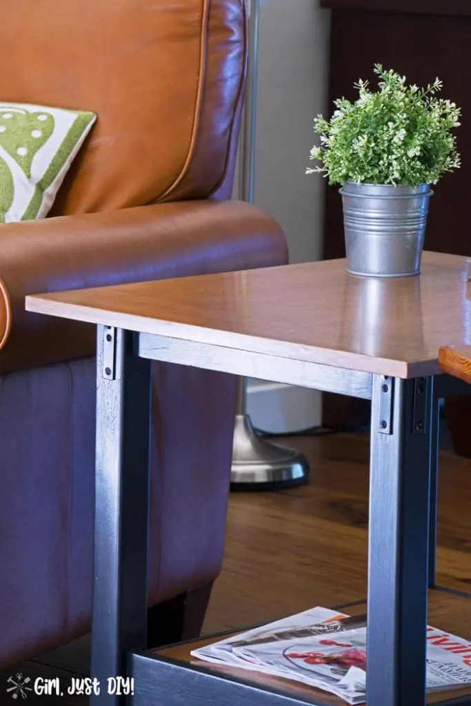 Closeup of DIY Industrial end table next to chair with green plant on top.