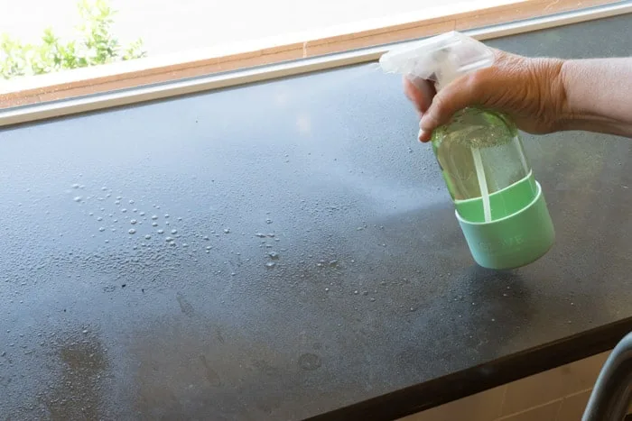 Hand spraying windowsill with bottle of window cleaner.