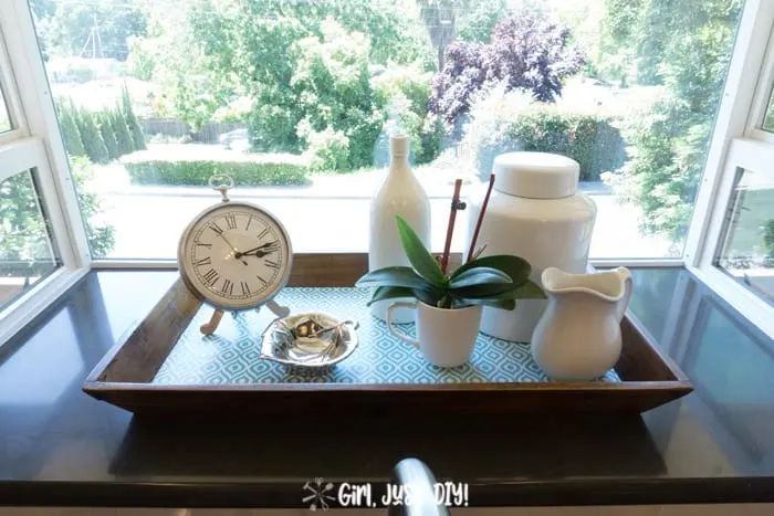 Wooden tray with contact paper bottom in window with ironstone and a clock.