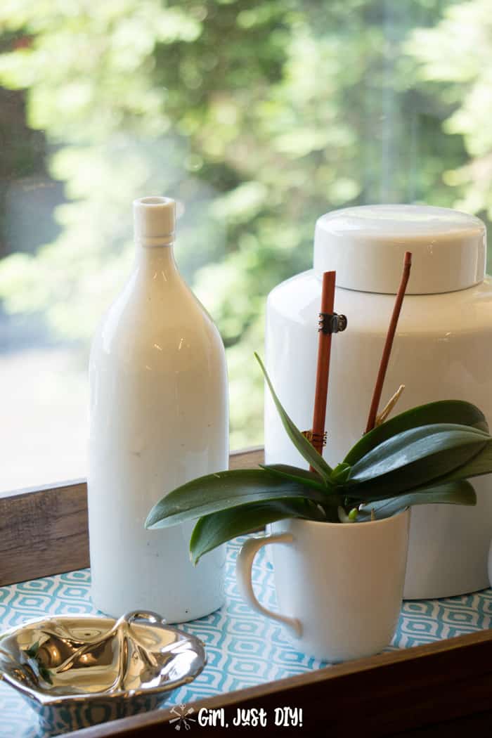 Wooden tray in window with enamelware and an orchid.