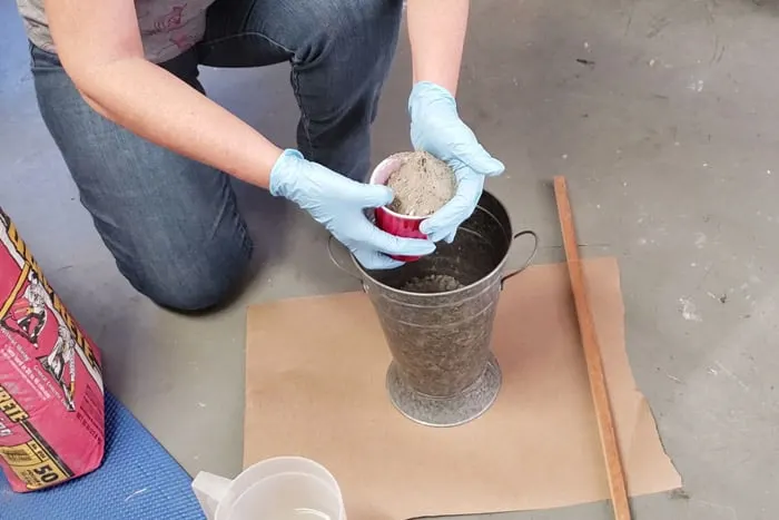 gloved hands adding mortar mix to galvanized bucket.