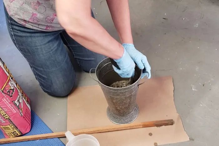 gloved hands stirring mortar and water with hand shovel.