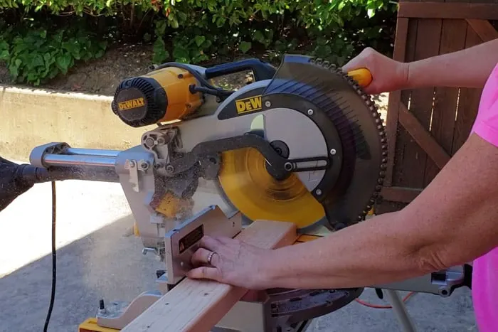 Dewalt brand Miter saw cutting through 2x4 board held by lady's hand.