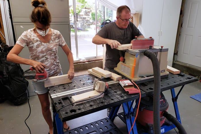 Man and woman standing at work table sanding pieces of 2x4.