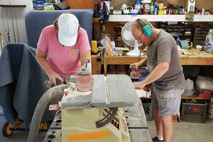 Woman and man standing at work bench sanding pieces of 2x4s