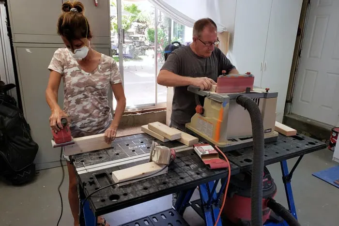 Man and woman still at work bench with power sanders sanding 2x4s.